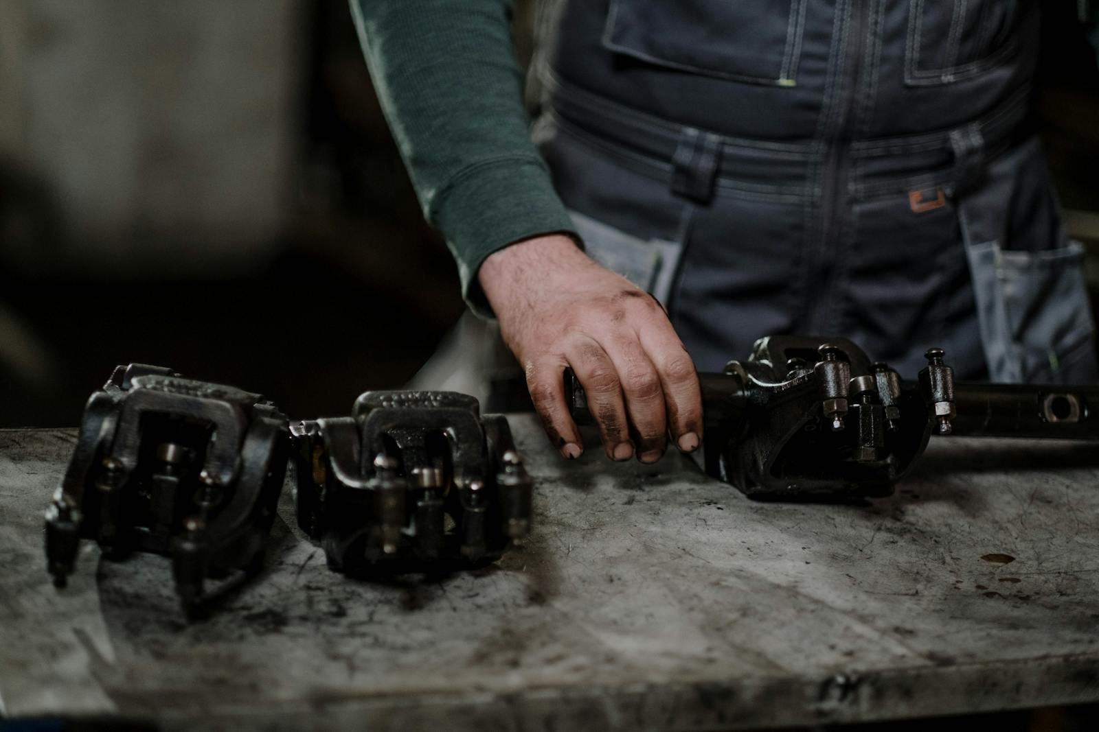 Gonzalez Carmona Contacto Urgente - Mechanic in workshop handling greasy metal parts on workbench, depicting repair process.